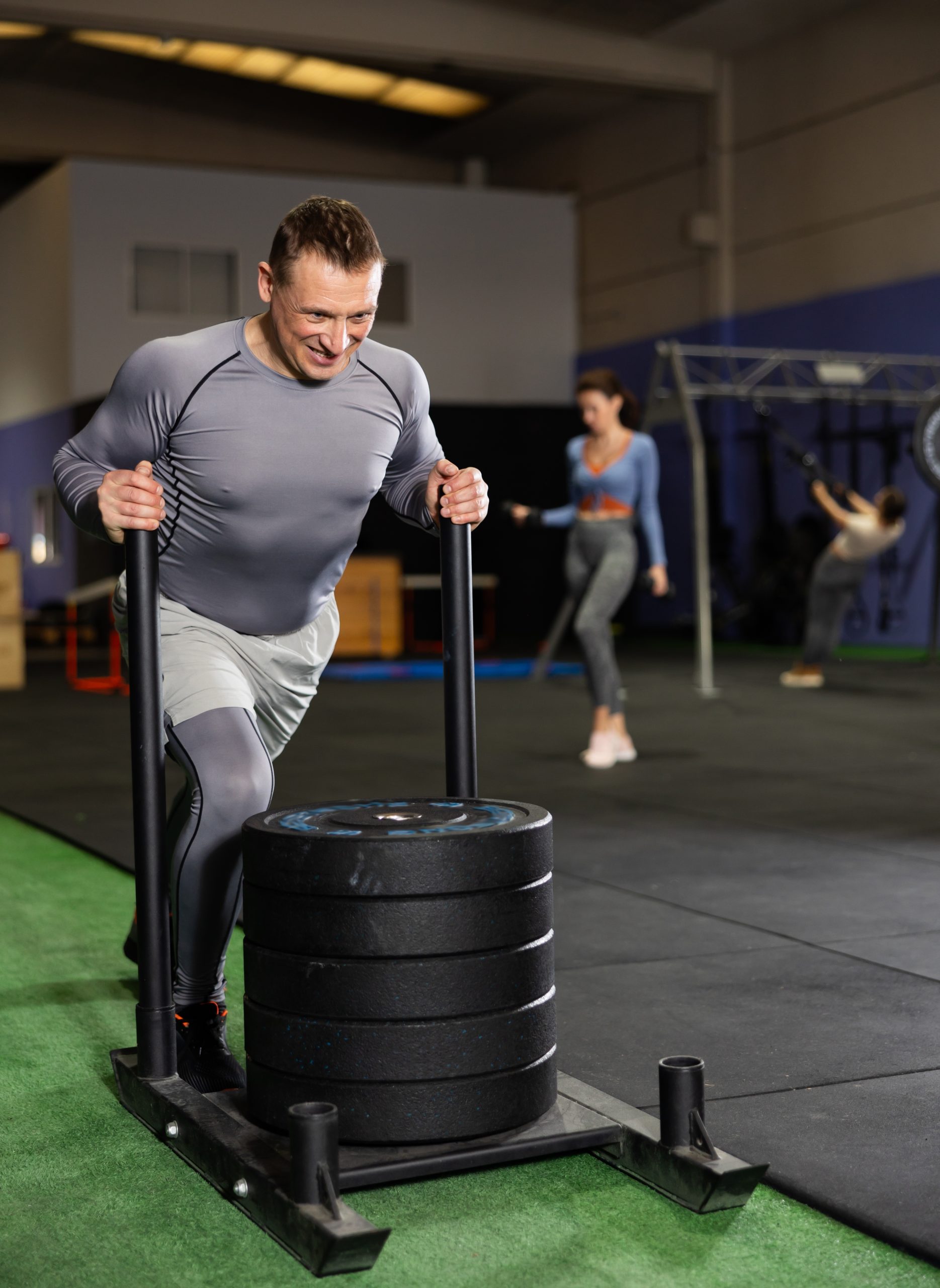 Determined,Middle-aged,Man,Pushing,Heavily,Loaded,Sled,Across,Gym,Floor,